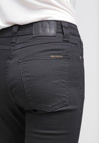 Svarta jeans i denim, med en slät yta, en bakficka med ett vågmönster och en läderetikett i midjan. Guldlogotyp som detalj.