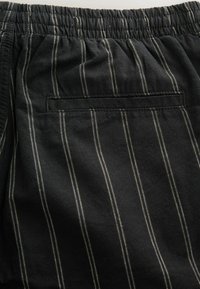 Schwarze Stoffshorts mit weißen vertikalen Streifen, ausgestattet mit einem elastischen Bund und einer Gesäßtasche mit sauberem Finish.