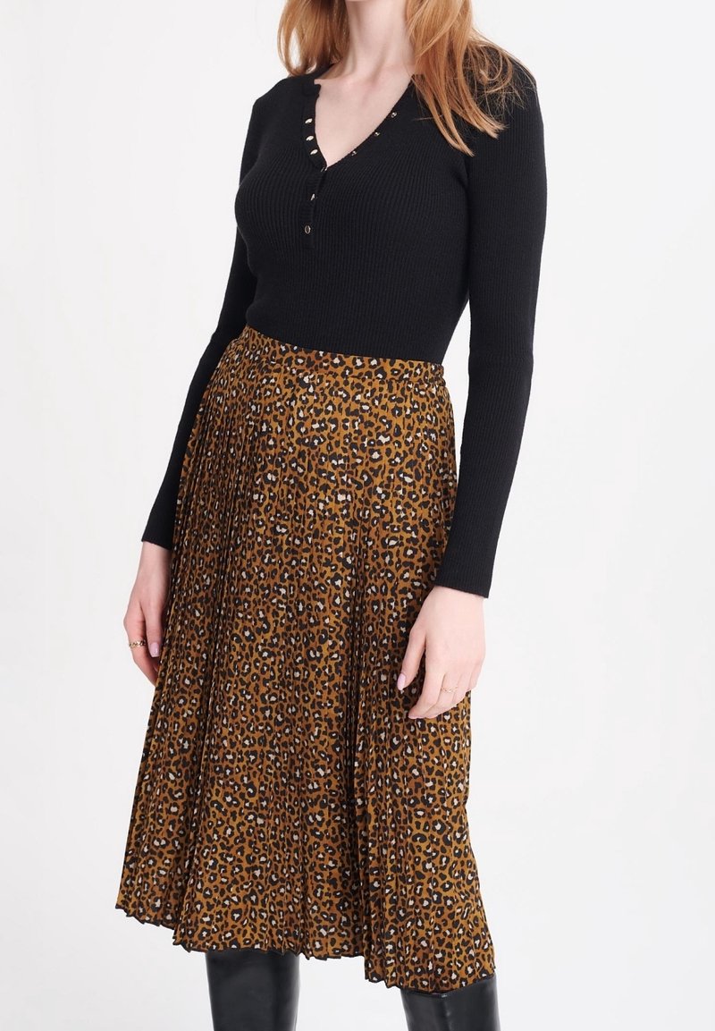 Kvinna som bär en svart långärmad ribbad topp och en mittlång plisserad kjol med ett brunt leopardmönster.