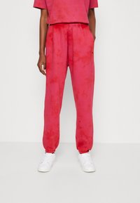 Lys rosa tie-dye svedpants med elastisk talje, tætsiddende pasform, sidelommer og ribbede манchetter, kombineret med en matchende top.