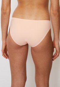 Perzikkleurige bikinionderkant met een gladde, elastische textuur en een eenvoudig ontwerp, met een lage taille en minimale bedekking.