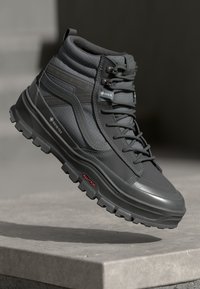 Mørk grå høyhælte støvler laget av teksturert materiale, med en robust såle, snøredesign og GORE-TEX merkevare på siden.