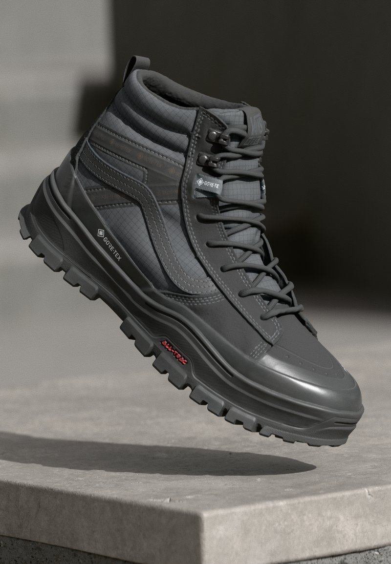 Botte montante gris foncé en matériau texturé, avec une semelle robuste, un design à lacets et un logo GORE-TEX sur le côté.