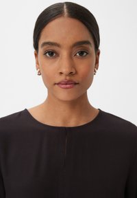 Black top with a round neckline and a subtle front slit. Smooth texture with a fitted design, worn by a person with dark, straight hair.