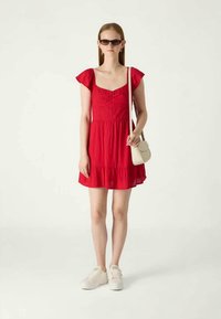 Red, short-sleeve, flared dress with a square neckline and gathered bodice. Paired with white sneakers and a small cream crossbody bag.