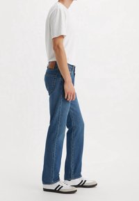 Lättviktig vit bomull t-shirt i kombination med urblekta blå raka jeans, med en brun läderetikett och avslappnade svarta och vita sneakers.