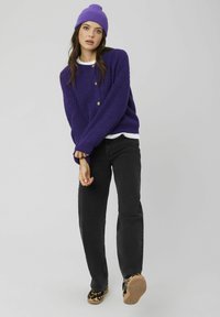 Pull en tricot violet à coupe décontractée avec détails de boutons, associé à un jean noir et des chaussures imprimé léopard. Le bonnet est assorti au pull.