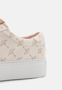 Beige lenkkari, jossa on teksturoitu pinta, jossa on lehden kaltaisia muotoja, valkoinen kumipohja ja huomaamattomat ruskeat yksityiskohdat kantapäässä.