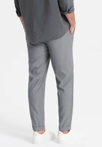 Grå skräddarsydda byxor med strukturerad tyg, slim fit och uppvikta benslut, kombinerat med vita sneakers på en enfärgad bakgrund.