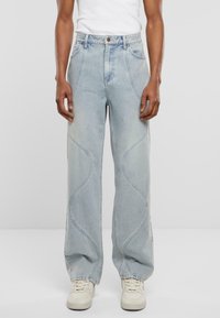 Jeans de mezclilla azul claro con un corte holgado, presentan detalles de costura curva y una cintura alta. Acompañados de zapatillas blancas.