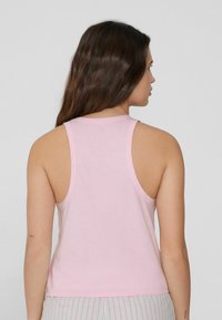 Różowy bawełniany top na ramiączkach z okrągłym dekoltem i plecami w stylu racerback. Materiał jest gładki, zapewnia dopasowany krój i swobodny wygląd.