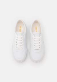 Ett par vita läder snörskor med sömdekor, sett ovanifrån på en enfärgad vit bakgrund.