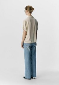 Kortärmad, ljusbeige blus med krage, tillsammans med ljusblå, löst sittande jeans. Outfitten inkluderar svarta spetsiga skor.