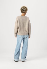 Beiger Wollmischpullover mit lockerer Passform, geripptem Kragen und Bündchen, kombiniert mit hellblauen Schlagjeans mit umgeschlagenen Säumen.
