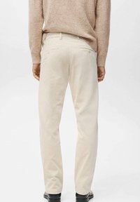 Pantalones de pana beige con un corte recto, que cuentan con bolsillos traseros y una textura suave. Combinados con un suéter beige claro.