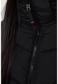 Chaqueta negra impermeable con textura acolchada, que cuenta con un cierre frontal y una etiqueta de logo cerca del cuello. El cierre es de un negro contrastante.