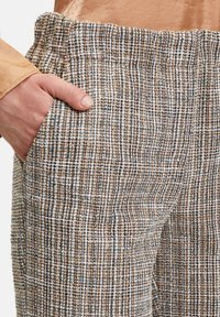 Trousers featuring a textured, multicolored woven pattern with browns, whites, and blues; an elastic waistband and side pockets.