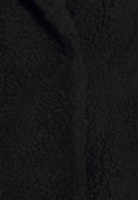 Tissu en polaire noir, pelucheux, présentant une surface texturée et bouclée avec une sensation douce. Idéal pour offrir chaleur et confort dans les vêtements d'extérieur.