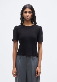 Μαύρο κοντομάνικο τοπ με υφή, με λαιμόκοψη σε σχήμα κυματιστού τελειώματος και ατελές τελείωμα, σε συνδυασμό με γκρι παντελόνες ψηλόμεσες.