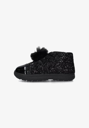 Sneaker alta nera glitterata con punta lucida, decorazione con pom-pom neri e lacci neri su uno sfondo bianco.