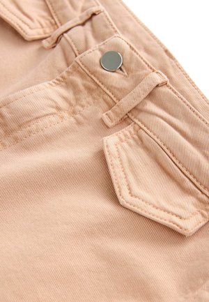 Ljusrosa denimtyg med en sydd ficka med en metallknapp och en liten bältesöggla, som visar ett strukturerat, ribbat mönster.