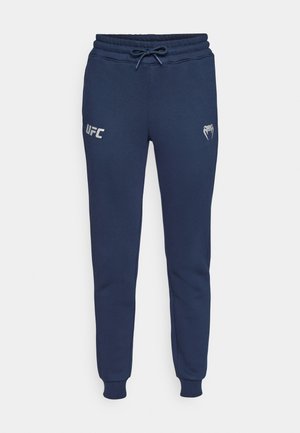 Mørkeblå joggebukser laget av myk stoff, med snøring i livet, ribbede mansjetter og trykt UFC-logo på venstre side.