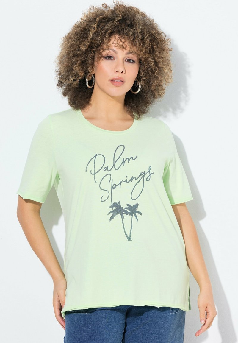 Světle zelené tričko s krátkým rukávem vyrobené z měkké tkaniny, se textem "Palm Springs" a grafikou palmy v tmavší barvě.