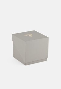 Boîte grise avec une texture, portant un logo triangulaire en or sur le dessus. La boîte comporte un couvercle qui chevauche légèrement la base avec des bords nets et angulaires.