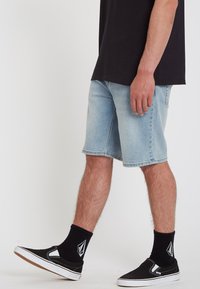 Light blue denim shorts with a straight-cut design, raw hem, five-pocket detailing, worn with black slip-on shoes and dark socks.
