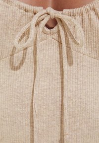 Tissu beige côtelé avec un décolleté en trou de clé, featuring une fermeture à cordon au col et un détail texturé dans le tissu.