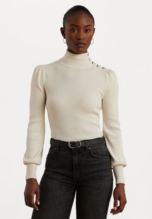 Maglione a collo alto a coste color crema con maniche a sbuffo, dettagli con bottoni laterali e design aderente, abbinato a jeans neri e a una cintura nera.