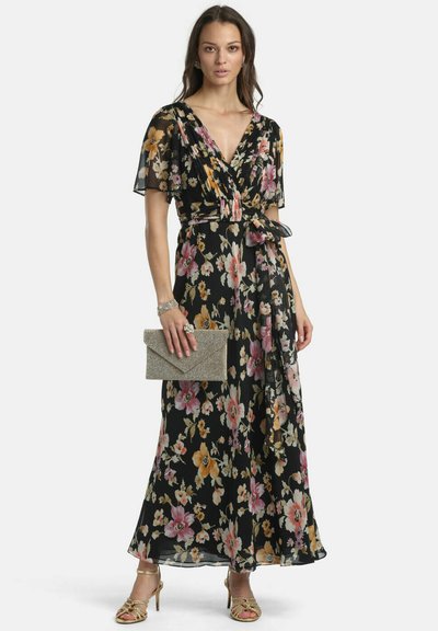 Woman wearing a black floral wrap dress with short sleeves, holding a glittery clutch, and wearing gold strappy heels and jewelry.