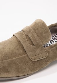 Mocassin en daim marron avec une bride à pièce penny et une semelle intérieure imprimée léopard visible à l'intérieur de la chaussure.
