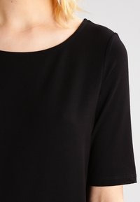 Czarny krótki top z rękawem, z okrągłym dekoltem. Gładki, miękki materiał z minimalnymi detalami szwów. Prosty i uniwersalny design.