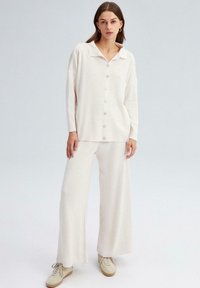 Conjunto de loungewear de punto acanalado en color crema, que incluye una parte superior con botones y cuello, y pantalones de pierna ancha. Textura suave y corte holgado.