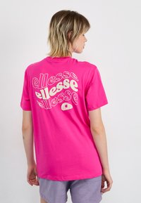 T-shirt en coton rose avec un logo "ellesse" de style rétro en blanc au dos. Manches courtes et coupe décontractée.