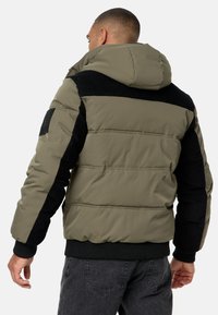 Veste à capuche en matière doudoune avec un design bicolore en olive et noir, accents en velours côtelé texturé, et poignets et ourlet côtelés.