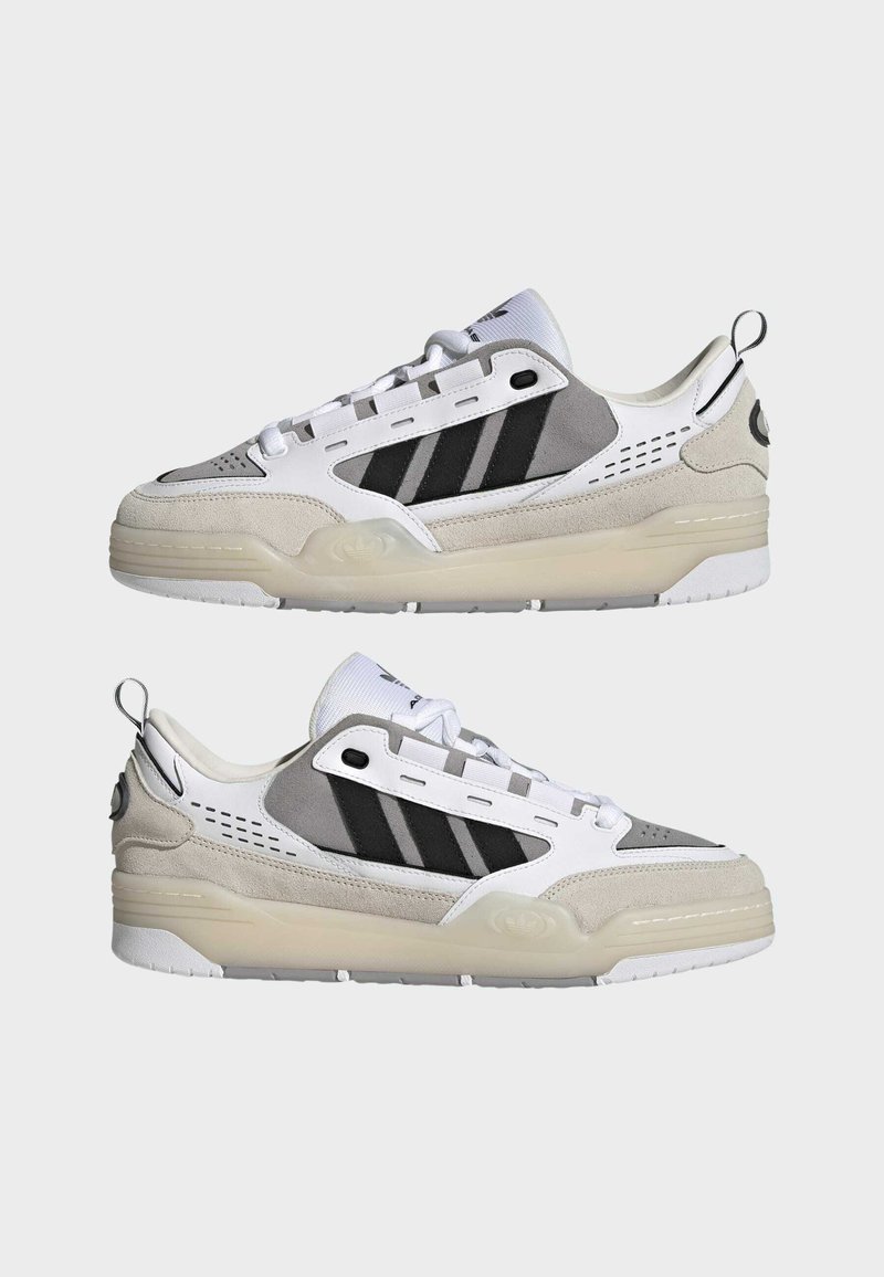 Sneakers z białą cholewką z szarymi i czarnymi akcentami, wykonane z zamszu i siateczki, z teksturowaną podeszwą oraz pętelką na pięcie.