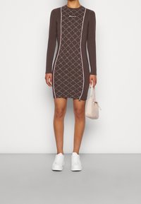 Brązowa sukienka z długim rękawem o dopasowanej sylwetce, zdobiona białymi i różowymi geometrycznymi wzorami. Połączona z białymi sneakersami i jasnoróżową torebką.
