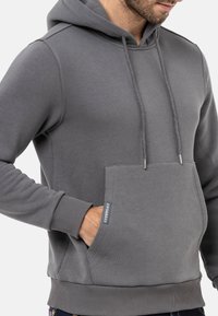 Grauer Kapuzenpullover mit Kordelzug, Fronttasche und gerippten Bündchen und Saum. Hergestellt aus glattem, weichem Stoff mit einem Logotag auf der Tasche.