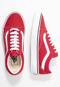 Paire de baskets basses rouges avec lacets blancs, bande latérale blanche et semelles en caoutchouc blanc, vues de dessus et de côté.