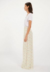 Jupe maxi en crème clair avec un motif floral en bleu, orange et vert. Tissu doux, silhouette en A et taille haute.