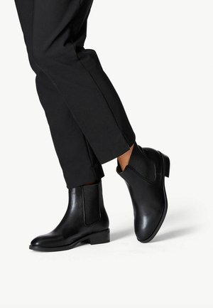 Black leather ankle boots with elastic side panels, a rounded toe, and a low block heel, paired with tailored black pants.