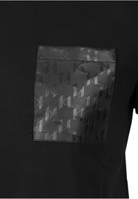 Black T-shirt featuring a textured black leather patch with a geometric pattern. The shirt has a crew neckline and short sleeves.