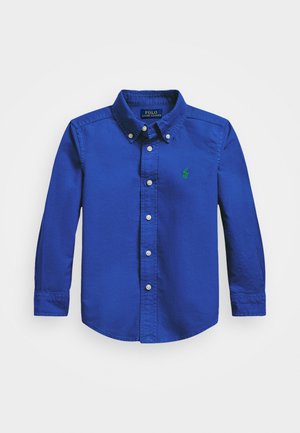 Langärmliges Hemd mit Knöpfen aus leuchtend blauem Baumwollstoff, mit einem grünen Logo auf der Brust, Kragen und klassischen Manschetten.