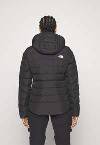 Crna izolirana puffer jakna s odvojivom kapuljačom, horizontalnim šavovima i logotipom North Face na gornjem dijelu leđa.