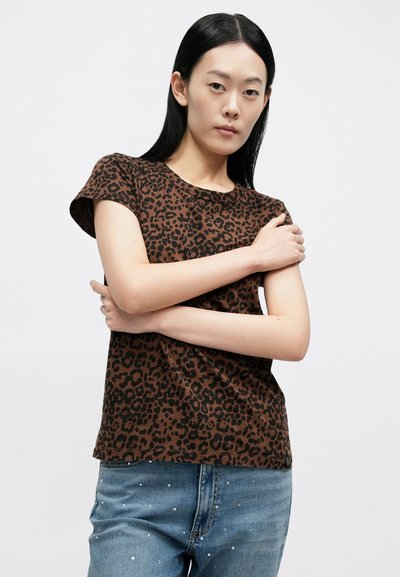 Brązowy t-shirt w panterkę z krótkimi rękawami, okrągłym dekoltem i luźnym krojem, zestawiony z niebieskimi jeansami z ozdobami.