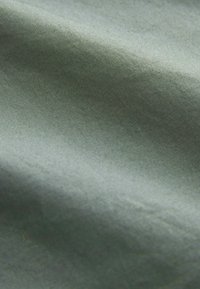 Tissu vert à texture lisse, présentant un léger éclat et de subtils motifs tissés, tombant doucement avec de légers plis.