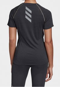 Zadní pohled na osobu ve černém krátkém rukávu sportovního trička s třemi diagonálními reflexními pruhy a černými legínami.