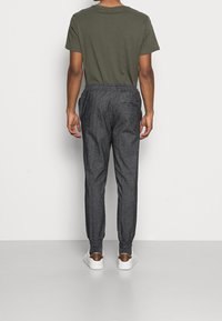 Pohodlné tmavě šedé tepláky volného střihu s elastickým pasem, bočními kapsami a jednou kapsou na zadní straně, doplněné o zelené tričko s krátkým rukávem a bílé tenisky.